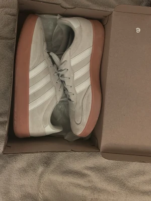 Adidas sneakers med vit mocka och gummisula - Snygga Adidas sneakers i vit mocka med klassiska tre ränder på sidan och en chunky ljusbrun gummisula. Skorna har snörning och låg profil, perfekt för en clean och stilren look. Adidas-logga på plösen och insidan. Grisch🍾🍾köptes för 1200kr och de är knapt använda