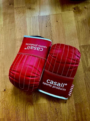 Röda boxningshandskar och svart boxningssäck från Casall - Säljer ett par röda boxningshandskar från Casall med vita detaljer och ränder. Handskarna har vadderad ovansida, vit insida och elastiskt rödvitt band runt handleden. Perfekta för träning eller kampsport. Svart boxningssäck ingår. Slitstarkt material och levereras med kedja och karbinhakar för upphängning. Perfekt för hemmaträning både för nybörjare och avancerade. 