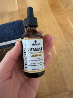 Vitamin E olja från Kanzy - Naturlig Vitamin E olja från Kanzy med pipett, perfekt för hud, hår och naglar. Innehåller mandel-, vetegrodds-, solros-, argan-, aprikos- och avokadoolja. Fri från kemikalier och 100% naturlig. Flaskan är brun med svart pipett och etikett.