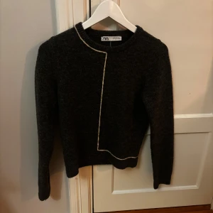 Mörkgrå stickad tröja från Zara - Mörkgrå stickad tröja från Zara med lång ärm och rund halsringning. Tröjan har en unik vit kontrastsöm som löper asymmetriskt framtill och baktill. Intr använd mycket.