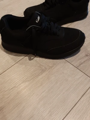 Svarta sneakers från GaitLine - Stilrena svarta sneakers från GaitLine med klassisk låg profil och snörning. Ovandelen är i textil och syntetmaterial, perfekt för en clean och sportig look. Passar till det mesta och är riktigt bekväma för vardagsbruk.