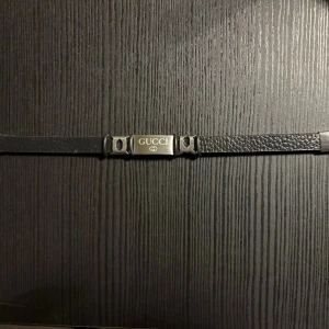 Armband  - Svart armband med silverbricka som har text på. Brun baksida. Spänne. Armbandet är ca 22 cm från spänne till spänne. Ring handleden är den ca 19cm. Endast tagit ut förpackning för att fota