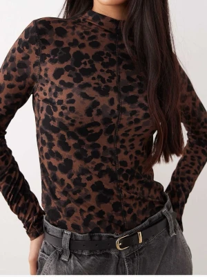 Leopardmönstrad långärmad topp - Snygg långärmad topp med leopardmönster i bruna och svarta toner. Toppen har en hög hals och figurnära passform, perfekt att styla med jeans eller kjol för en trendig look.