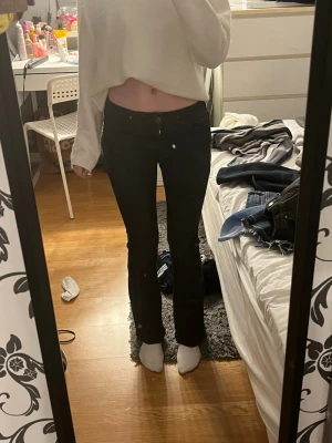 Svarta bootcut jeans - Säljer ett par svarta bootcut jeans med klassisk femficksdesign och låg midja. Jeansen har en snygg passform som sitter tight upptill och släpper ut vid benen. Perfekta för dig som gillar en stilren och tidlös look.