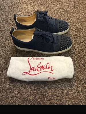 Marinblåa Christian Louboutin sneakers - Säljer ett par marinblåa sneakers från Christian Louboutin i mocka med coola nitar på tån. Skorna har vita sulor och klassisk snörning. Perfekta för dig som vill sticka ut med en edgy och lyxig stil.