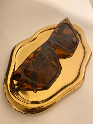 Bruna fyrkantiga solglasögon - Snygga solglasögon med fyrkantig form och trendigt sköldpaddsmönster i bruna toner. Bågarna är i plast och ger en cool retrovibe. Perfekta för att lyfta din stil under soliga dagar.