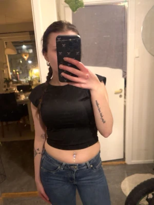 Svart croppad ärmlös topp - Säljer en svart croppad topp med breda axelband och rund halsringning. Toppen är ärmlös och har en enkel, stilren design som passar perfekt till jeans eller kjol. Materialet känns mjukt och följsamt mot kroppen.