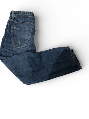 Blå jeans från Jack & Jones, regular fit - Säljer ett par klassiska blå jeans från Jack & Jones i regular fit. Jeansen har raka ben, fem fickor och snygga kontrastsömmar. Tillverkade i slitstarkt denim med en cool tvättad look. Perfekta för dig som gillar en tidlös och avslappnad stil.