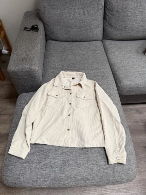 Beige overshirt i manchester - Snygg beige kappa i mjuk manchester med klassisk krage och två bröstfickor med lock. Långa ärmar med knapp vid ärmslut och knäppning framtill. Köpt på shein, storlek Xs. Aldrig andvänd.