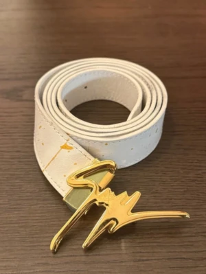 Vitt skärp med guldspänne från Giuseppe Zanotti - Snyggt vitt skärp från Giuseppe Zanotti med unikt guldspänne i signaturdesign. Skärpet har små guldstänk som ger en cool touch och är gjort i skinn. Perfekt accessoar för att lyfta din outfit. Finns repor på spännet. 