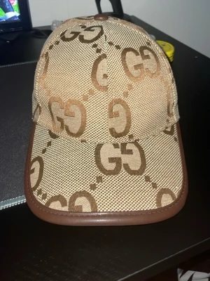 Beige keps med GG-mönster från Gucci - äljer en snygg beige GG-keps i bruna toner. Bekväm att ha på sig och sitter bra, med lätt böjd skärm. Funkar till det mesta och är lätt att matcha. Använd men fortfarande i fint skick. Säljs pga kommer inte till användning längre.