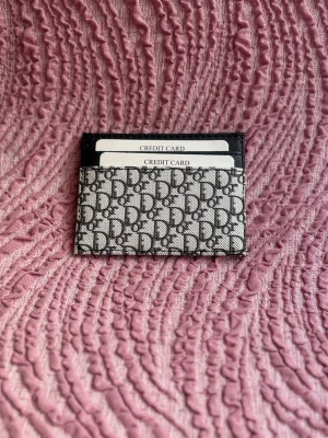  korthållare i monogramtyg - Snygg korthållare i  svart och grått monogramtyg. Plånboken har flera fack för kort och den klassiska  över hela framsidan. Perfekt för dig som vill ha en stilren och lyxig accessoar i fickan.