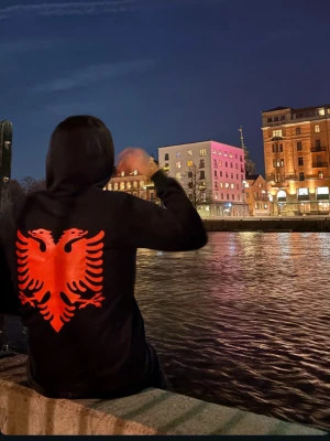 Alban kofta - Säljer en svart hoodie med stor röd dubbelhövdad örn på ryggen och ett mindre rött tryck på bröstet. Hoodien har huva och en klassisk passform. Perfekt för dig som vill sticka ut med en unik design.