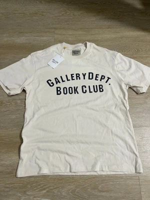 Vit t-shirt  - Snygg vit t-shirt  Book Club' i svart på bröstet. Klassisk rund hals och korta ärmar. Tillverkad i mjuk bomull som känns skön mot huden. Perfekt för dig som gillar streetwear och enkel stil.