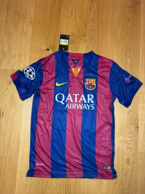 FC Barcelona Neymar Jr matchtröja - Säljer en officiell FC Barcelona matchtröja från Nike med Neymar Jr och nummer 11 på ryggen. Tröjan har breda blå och vinröda ränder, Champions League-patchar på ärmarna och Qatar Airways-tryck på bröstet. Tillverkad i lätt och ventilerande polyester.