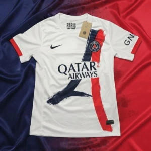 PSG  fotbollströja - Snygg vit PSG fotbollströja från Nike med tryck i marinblått och rött, samt klubbmärke på bröstet. Tröjan har korta ärmar med röda detaljer och är tillverkad i lätt, ventilerande material. Perfekt för dig som vill representera Paris Saint-Germain.