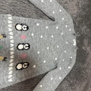 Grå jultröja med pingviner från H&M - Supermysig grå stickad jultröja från H&M med söta pingviner, renar och granar nertill. Tröjan har vita prickar som ser ut som snö och rosa snöflingor. Långärmad och perfekt för vinterns alla tillfällen.