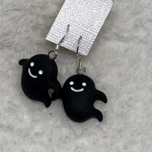 Svarta spökörhängen halloween  - Unika örhängen med svarta spöken som har vita leenden och ögon. Perfekt accessoar för dig som gillar lekfulla och annorlunda smycken. Hängande modell som verkligen sticker ut och ger en cool touch till din stil. Krokarna är i sterling silver 