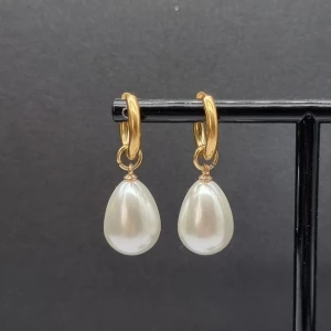 Guldiga örhängen med pärldroppar - Snygga örhängen med rundad guldfärgad ring och droppformad vit pärla som hänger ned. Material-rostfritt stå. 