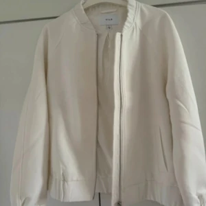 Vit bomberjacka från Vila - Snygg vit bomberjacka från Vila med dragkedja framtill och ribbade muddar. Jackan har en clean look och är perfekt för dig som gillar minimalistisk stil. Lätt vadderad och med två fickor på sidorna. Passar till det mesta och är enkel att matcha.