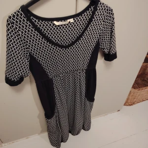 Svartvit House of Lola kortklänning XS - Snygg kortklänning från House of Lola i svart och vitt med grafiskt rutmönster. Klänningen har rund hals, korta ärmar och praktiska fickor på sidorna. Materialet känns mjukt och stretchigt, perfekt för dig som gillar bekväma och coola plagg.