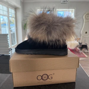 Svarta boots med päls från OOG Generation - Säljer ett par svarta boots från OOG Generation med fluffig beigegrå päls upptill. Skorna har rund tå och platt sula, tillverkade i mocka med en metallplatta bak. Perfekta för att hålla stilen under kyliga dagar.