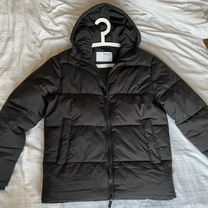 Vinterjacka - Säljer en svart pufferjacka från Selected Homme med huva och dragkedja. Jackan har två stora fickor framtill, en innerficka och är vadderad för extra värme. Perfekt för kyliga dagar och enkel att matcha med olika outfits.