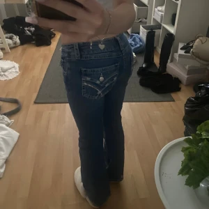 Blå bootcut jeans från Gina Tricot - Säljer ett par blå jeans från Gina Tricot i modell bootcut med snygga detaljer på bakfickorna. Jeansen har låg midja och klassisk femficksdesign. Materialet är jeans med en skön passform och coola sömmar på fickorna.