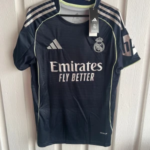 Real Madrid Mastantuono matchtröja - Snygg mörkblå Real Madrid fotbollströja från Adidas med Mastantuono och nummer 30 på ryggen. Tröjan har korta ärmar, silverfärgade ränder på axlarna och klubbmärke på bröstet. Tillverkad i lätt funktionsmaterial med Aeroready-teknologi.