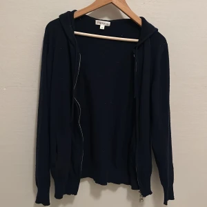 Mörkblå cashmere hoodie från Barlucio - Mörkblå cashmere hoodie från Barlucio i storlek S. Tröjan har dragkedja framtill, huva och långa ärmar. Perfekt för dig som gillar en enkel och stilren look. Materialet känns mjukt och passar bra till kyligare dagar.