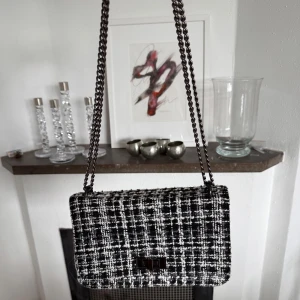 Rutig axelväska  - Snygg axelväska från Primark i svart och vitt rutigt tyg med grov struktur. Väskan har en metallkedja som axelrem och ett stilrent lås framtill. Perfekt storlek för det viktigaste.