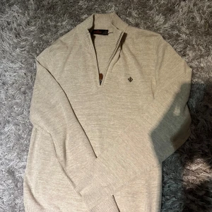 Halv zip från morris - Beige stickad tröja från Morris med half zip och snyggt broderad logga på bröstet. Tröjan har ribbade muddar, hög krage och dragkedja med läderdetalj. Perfekt för lager-på-lager under höst och vinter. Pris 900kr👍 storlek M | har inga defekter. 