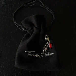 Thomas Sabo charm med par och paraply - Unik charm från Thomas Sabo i silverfärgad metall, föreställande ett kärlekspar som kysser under ett rött paraply. Baksidan har texten 'Soul Mate'. Perfekt att hänga på armband eller halsband.