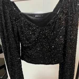 Svart paljettopp från Gina Tricot (pris kan diskuteras) - Glittrig svart topp från Gina Tricot med långa ärmar och croppad passform. Hela toppen är täckt av svarta paljetter som ger en riktigt festlig look. V-ringad framtill och figurnära modell som verkligen sticker ut.