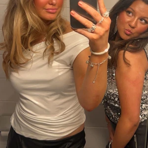 Vit offshoulder topp - Säljer en snygg vit offshoulder topp med glansig finish. Toppen har en tight passform och är tillverkad i ett syntetmaterial som ger en cool och modern look. Perfekt för dig som vill sticka ut med en stilren och trendig outfit.