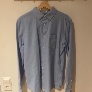 Blå slim fit skjorta från Primark - Snygg ljusblå skjorta från Primark i slim fit-modell, tillverkad i 100% bomull. Skjortan har klassisk krage, knappar framtill och en bröstficka. Perfekt för dig som gillar stilrena och enkla plagg med bra passform.