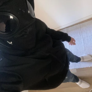 Svart hoodie med glasögon i huvan - Säljer en svart hoodie med hel dragkedja och unika glasögon integrerade i huvan. Tröjan har en clean look, normal passform och är perfekt för dig som vill sticka ut. Tillverkad i mjuk bomullsmix och har klassiska muddar vid ärmslut och midja.