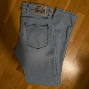 Ljusblå Replay Anbass jeans - Säljer ett par ljusblå Replay Anbass jeans med klassisk femficksdesign och snygga detaljer på bakfickorna. Jeansen har smal passform och är tillverkade i mjukt denimtyg med stretch för extra komfort. 