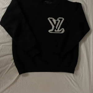 Svart stickad tröja från Louis Vuitton - Svart stickad tröja från Louis Vuitton med stort vitt LV-logo på både fram- och baksidan. Tröjan har rund halsringning och långa ärmar. Perfekt för dig som vill ha en klassisk men ändå lyxig look.