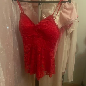 Röd spetsig linnetopp med volang - Säljer en röd linnetopp med tunna axelband och v-ringad hals. Toppen är helt täckt av spets och har en volang nedtill som ger en extra feminin touch. Perfekt för dig som vill sticka ut med en färgstark och snygg look. Storlek står ej, men gissar på S. 