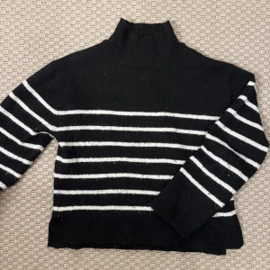 Svartvit randig polotröja - Säljer en svart stickad polotröja med vita horisontella ränder. Tröjan har hög krage och långa ärmar med breda muddar. Perfekt för dig som gillar klassisk stil med en modern twist.