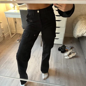 Svarta cargopants med raka ben ifrån Zara  - Säljer ett par svarta cargopants med raka ben och hög midja. Byxorna har flera praktiska fickor på sidorna och baktill, samt stängs med knapp och dragkedja. Materialet känns som bomull och de har en loose passform som ger en avslappnad vibe. Använda 1 gång🖤