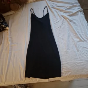 Svart klänning med smala axelband FB Sister - En stilren svart klänning från FB Sister i storlek S. Klänningen har smala axelband och en rak, kroppsnära passform som slutar ovanför knäna. Perfekt för dig som gillar minimalistisk och enkel stil. Materialet känns mjukt och följsamt mot kroppen.