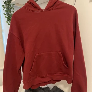 Mörkröd hoodie  - Enkel och snygg mörkröd hoodie med huva och stor magficka framtill. Tröjan har långa ärmar och ribbade muddar vid ärmslut och nederkant. 