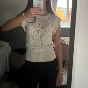 Vit stickad topp från Lindex - Säljer en söt vit stickad topp från Lindex i storlek S. Toppen har ett fint hålmönster, volangdetaljer vid ärmarna och bred ribbad kant nedtill. 💕