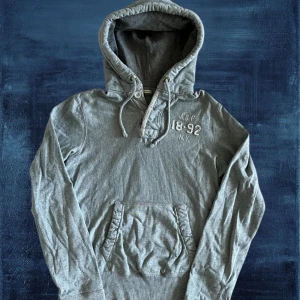 Abercrombie Fitch - Säljer nu denna riktigt snygga hoodien från Abercrombie Fitch. Bra skick. Modellen är 183, 67kg. Längd: 63,5, bredd: 50, arm: 67. OBS, Storlek L men uppskattar det mer som en M i storlek, kolla mått. lite slitage vid luvan osv, men inget som påverkar hoodien mycket alls. Skriv vid frågor