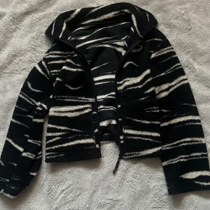 Svart teddyjacka med vita ränder - Säljer en svart teddyjacka med vita, oregelbundna ränder som ger en cool och unik look. Jackan har dragkedja framtill och är tillverkad i mjukt fleece-material. Perfekt för dig som gillar streetstyle och vill ha något som sticker ut. Ge ert prisförslag❤️
