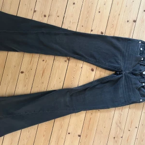 True Religion Joey Low Rise Flare Jeans - Snygga mörkgrå jeans från True Religion, modell Joey Low Rise Flare. Byxorna har låg midja, utsvängda ben och coola fickdetaljer bak. Materialet är en mix av bomull, polyester och lite stretch för extra komfort. Perfekta för dig som gillar en avslappnad men trendig look.