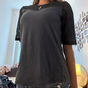 mörk blå blus med spetsdetaljer - Snygg Mörl blå blus med halvtransparent spets över axlar och ärmar. Rund halsringning och korta ärmar med spets som ger en cool touch. Perfekt att styla med jeans eller kjol för en trendig look. Materialet känns mjukt och lätt mot huden.