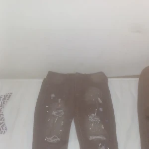 Svarta jeans med slitningar och färgstänk - Svarta jeans med coola slitningar och vita färgstänk på benen. Rå och trendig look med trasiga detaljer på knäna. Perfekta för dig som gillar streetstyle och vill sticka ut lite extra.